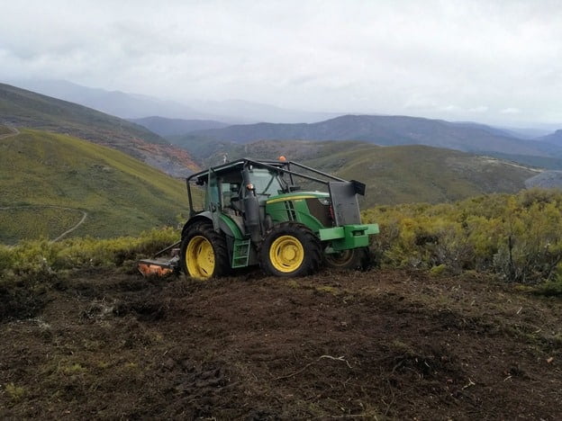 Tractor verde desbrozando un camino en pendiente